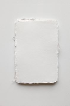 a square piece of white paper with torn edges on a white surface, viewed from above