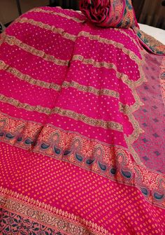 The saree is crafted from high-quality fabric that drapes beautifully and feels luxurious against the skin. The combination of the Bandhni tie-dye technique and the rich zari border creates a stunning visual contrast, making the saree both eye-catching and timeless. Elevate your style with this exquisite rani pink saree, featuring intricate Bandhni tie-dye patterns and stunning Jharokha Meenakari work. The elegant zari border adds a touch of opulence, making it a perfect choice for weddings and festive occasions. Experience timeless beauty and traditional craftsmanship with this vibrant and regal saree. SILK MARK CERTIFIED This saree is ready to wear with fall and pico done. Handmade silk tassels adorn the pallu and add more grace to it. An unstitched blouse fabric is included. *Note: Ther Pink Silk Bollywood Pre-draped Saree, Bollywood Style Jamawar Pre-draped Saree For Diwali, Festive Pre-draped Saree With Traditional Patterns, Pink Bollywood Pre-draped Saree With Zari Work, Pink Bandhani Print Pre-draped Saree For Festivals, Pink Pre-draped Saree With Zari Work For Eid, Pink Bollywood Silk Pre-draped Saree, Pink Bollywood Style Pre-draped Silk Saree, Bollywood Style Jamawar Pre-draped Saree