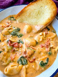 a white plate topped with pasta and spinach next to a piece of bread on top of a table