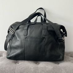 This Is A Stylish, Large Pebbled Leather Weekender From Cole Haan. It Has Been Lightly Used And Well Cared For. It Is Very Spacious With Two Zippered Pockets Inside And A Sturdy Zippered Enclosure Outside. The Base Is 20” Wide And 7” Deep. The Full Height From Top To Bottom Is 16 1/2”. Designer Black Duffle Bag For Everyday Use, Chic Black Weekender Bag With Luggage Sleeve, Elegant Black Weekender Bag With Leather Lining, Black Soft Leather Duffle Bag, Elegant Black Leather Travel Bag, Classic Black Weekender Bag With Leather Backing, Black Leather-lined Satchel Weekender Bag, Black Textured Leather Weekender Bag For Travel, Black Leather Weekender Bag For Business