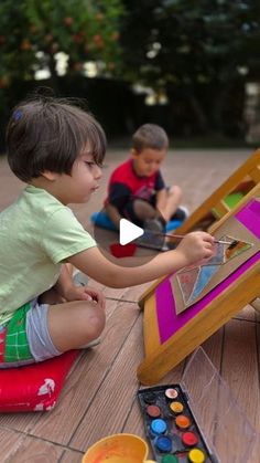 two young boys sitting on the ground playing with an easel