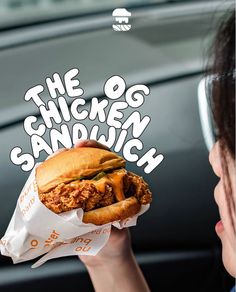 the chicken sandwich is being held up by a woman's hand in front of her car