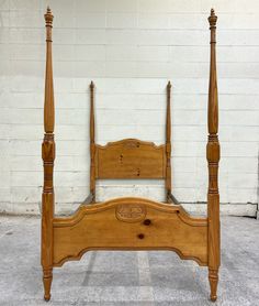 a wooden bed frame with four posts in front of a white brick wall and floor