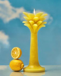 a yellow vase with a lemon and a candle in it sitting next to an orange