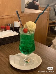 a green drink with ice cream and a cherry on the rim sitting on a table