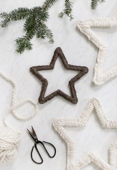 two knitted stars next to scissors on a white marble surface with evergreen branches and pine cones