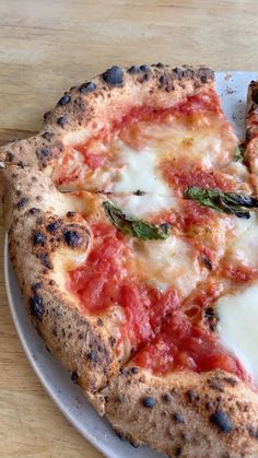 a pizza with cheese and tomato sauce on a white plate sitting on a wooden table