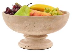 a bowl filled with fruit sitting on top of a white countertop next to a banana, pears and grapes