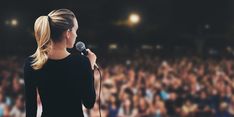 a woman standing in front of a microphone with an audience behind her at a concert