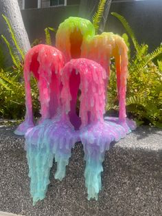 three brightly colored plastic sculptures sitting on top of a cement wall next to green plants