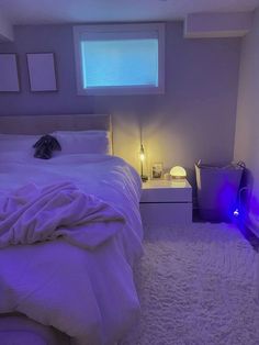 a white bed sitting in a bedroom next to a window with purple lights on it