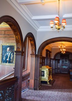 an ornate hallway with chandeliers and paintings on the walls, along with carpeted stairs