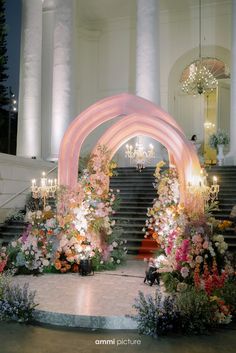 an archway decorated with flowers and chandeliers in front of a staircase at night