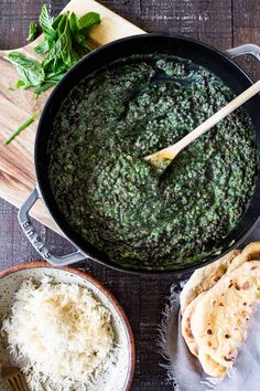 a pan filled with spinach and rice on top of a wooden table next to two bowls