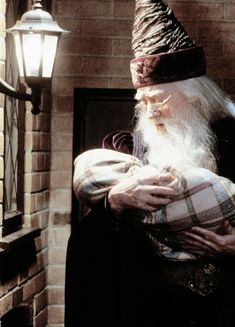 an old man holding a baby in front of a fire place with a wizard hat on