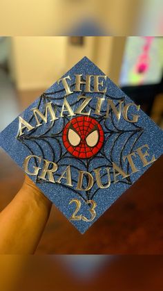 a hand holding up a blue graduation cap that says the amazing graduate 23 on it