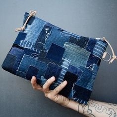 a hand holding a blue patchwork purse on top of a gray wall with writing all over it