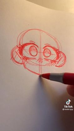 someone is drawing a face on paper with a red marker and there is a pencil in the foreground