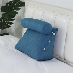 a blue pillow sitting on top of a bed next to a white headboard and plant