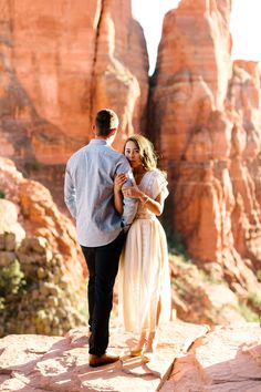 a man and woman standing in front of red rocks with their arms around each other