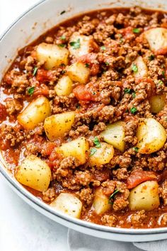 a white bowl filled with meat and potatoes on top of a table next to a spoon