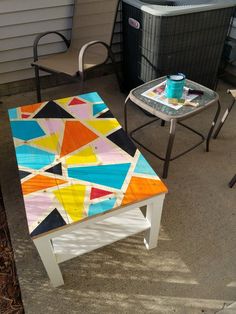 an outdoor table painted with different colors and shapes on the top, next to two chairs