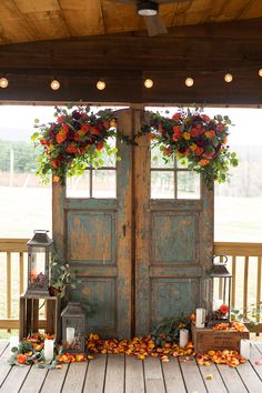 an old wooden door decorated with flowers and greenery on a porch for a fall wedding