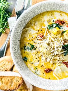 a white bowl filled with pasta and spinach soup next to slices of bread on a cutting board