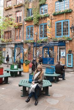 a woman sitting on top of a green bench in front of a tall brick building