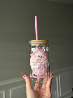 a person holding up a pink cup with a skeleton on it and a straw in its mouth