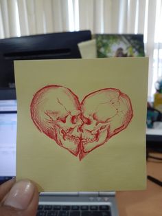 a hand holding up a piece of paper with two skulls in the shape of a heart