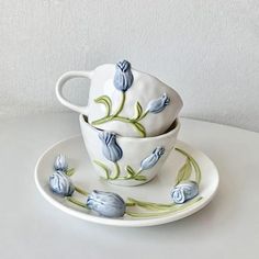 two cups and saucers with blue flowers painted on them sitting on a white table