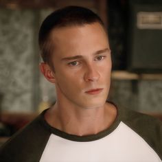 a man in a green and white t - shirt looks at the camera with serious look on his face