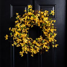 a wreath with yellow flowers hanging on a black door