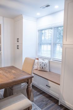 a wooden table sitting in front of a window next to a white cabinet and bench