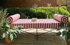 a red and white striped couch sitting on top of a patio next to potted plants