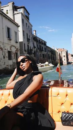 a woman sitting on top of a yellow couch next to a body of water with buildings in the background