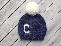 a knit hat with the letter c on it and a pom - pom