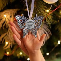 a hand holding a silver butterfly ornament in front of a christmas tree