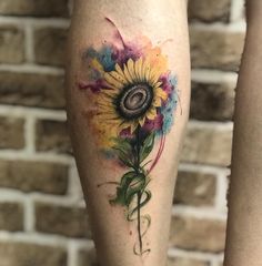 a sunflower tattoo on the leg with watercolor paint splatters around it