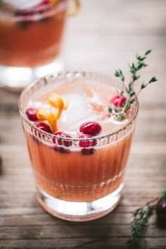 two glasses filled with drinks sitting on top of a wooden table next to berries and herbs