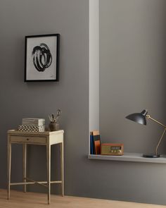 a desk with a lamp and books on it in front of a gray painted wall