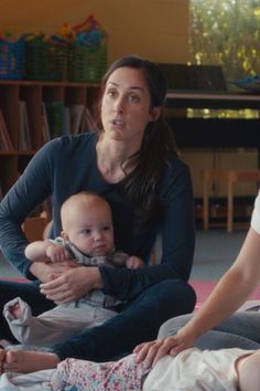 a woman sitting on the floor holding a baby in her lap while two other people sit nearby