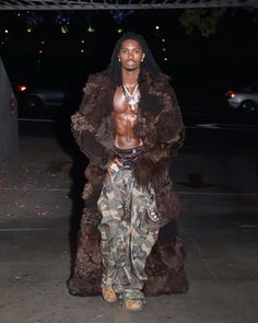 a man with dreadlocks standing in front of a car wearing a fur coat