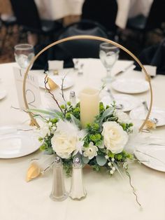 a centerpiece with white flowers and greenery on a table