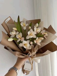 a person holding a bouquet of flowers in front of a white wall with a tag on it