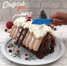 a gingerbread house is decorated with icing and christmas decorations on a white plate