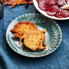 two pieces of fried chicken on a plate with beets and carrots in the background