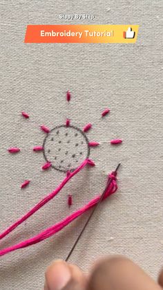 someone is stitching something on the fabric with pink thread and needles to make an embroidered sunburst