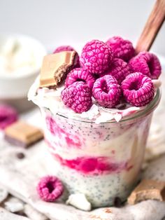 a dessert with raspberries and whipped cream in a glass jar on a table